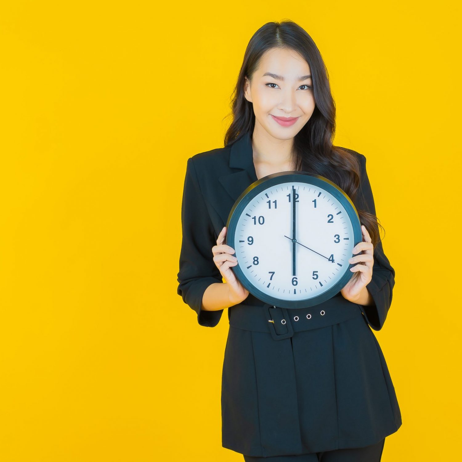 Portrait beautiful young asian woman show alarm or clock on yellow color background