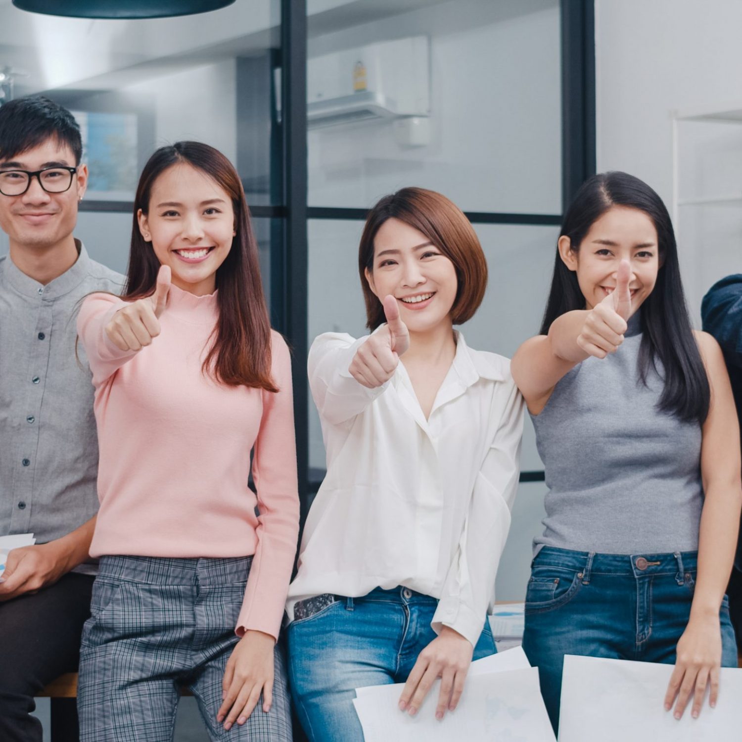 Group of Asia young creative people in smart casual wear smiling and thumbs up in creative office workplace. Diverse Asian male and female stand together at startup. Coworker teamwork concept.