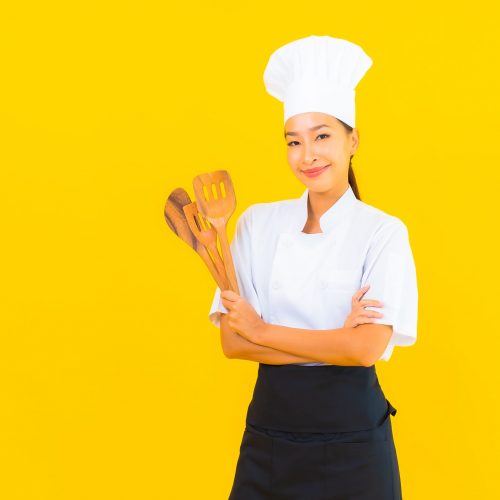 Portrait beautiful young asian chef woman with spatula on yellow isolated background